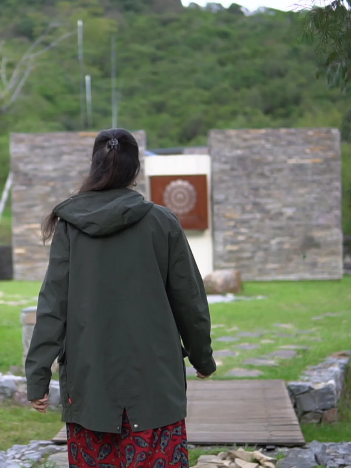 Participante de espaldas caminando hacia la entrada de piedra de la sede, con el cerro al fondo